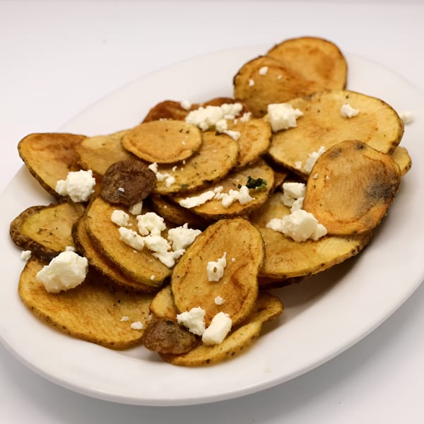 Crispy house-made potato chips topped with crumbled feta cheese on a white plate.