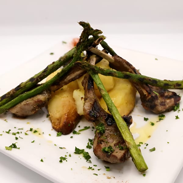 Grilled lamb chops with roasted potatoes and asparagus, garnished with parsley on a white plate.