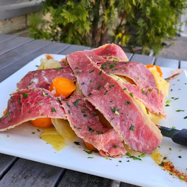 Thinly sliced corned beef with cabbage and carrots, garnished with parsley on a white plate.