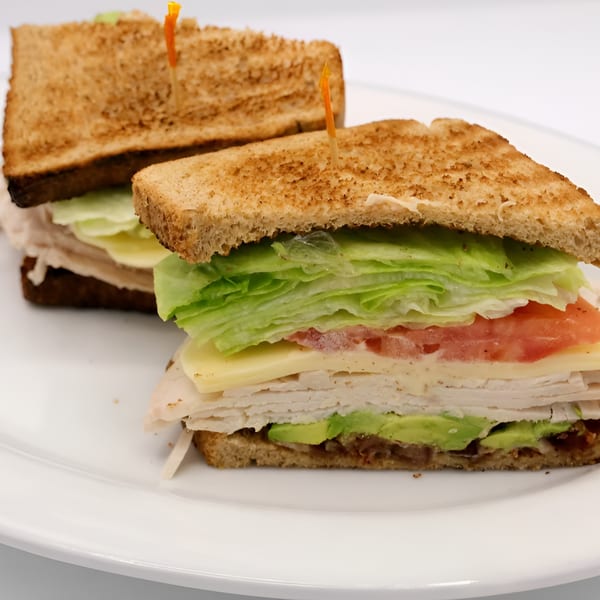 Two Montclair House Grill club sandwiches with turkey, avocado, cheese, lettuce, and tomato on toasted bread.